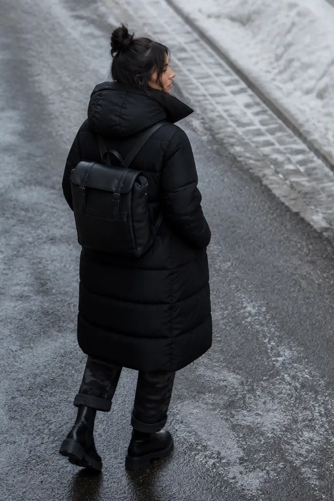 An elevated winter street look: black longline puffer coat over dark camo pants with cuffed hems, plus black chunky boots and a structured backpack.