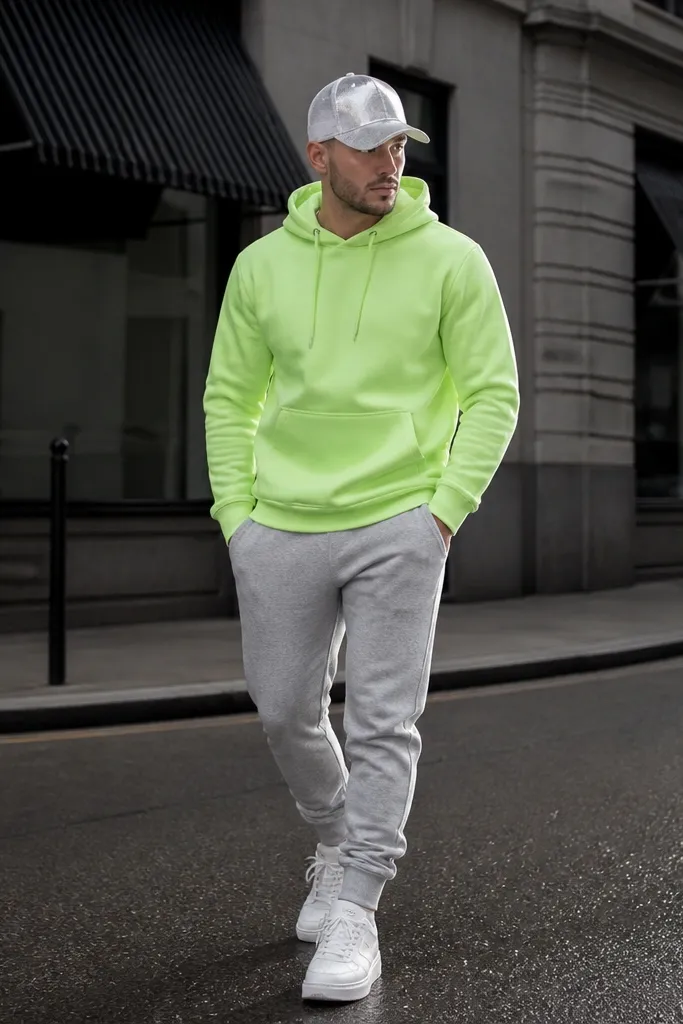 Man in a neon green hoodie over monochrome joggers, wearing a reflective cap and white sneakers; street background with flash-like highlights.