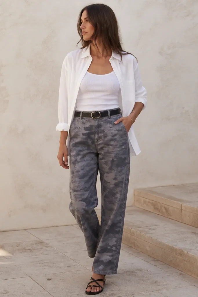 Grey camo pants styled with black leather strap sandals, a white linen button-up worn open over a fitted top, and a black leather belt at the waist.