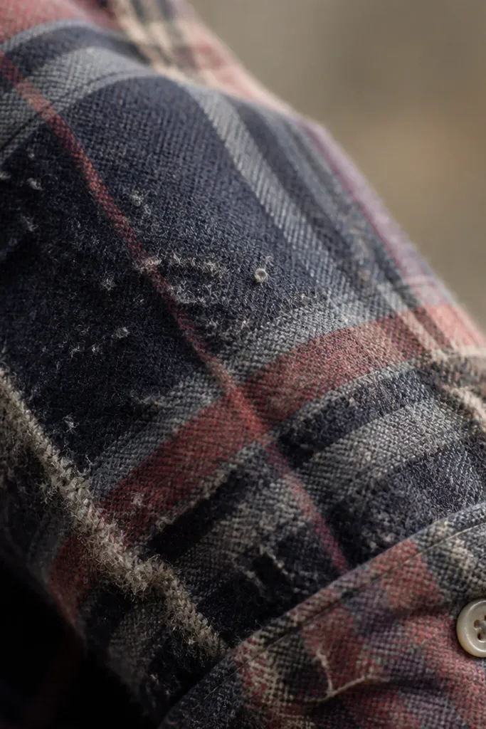 Close-up of a flannel sleeve showing fuzzy pills on the surface and lint clinging around seams; the fabric looks worn and rough.