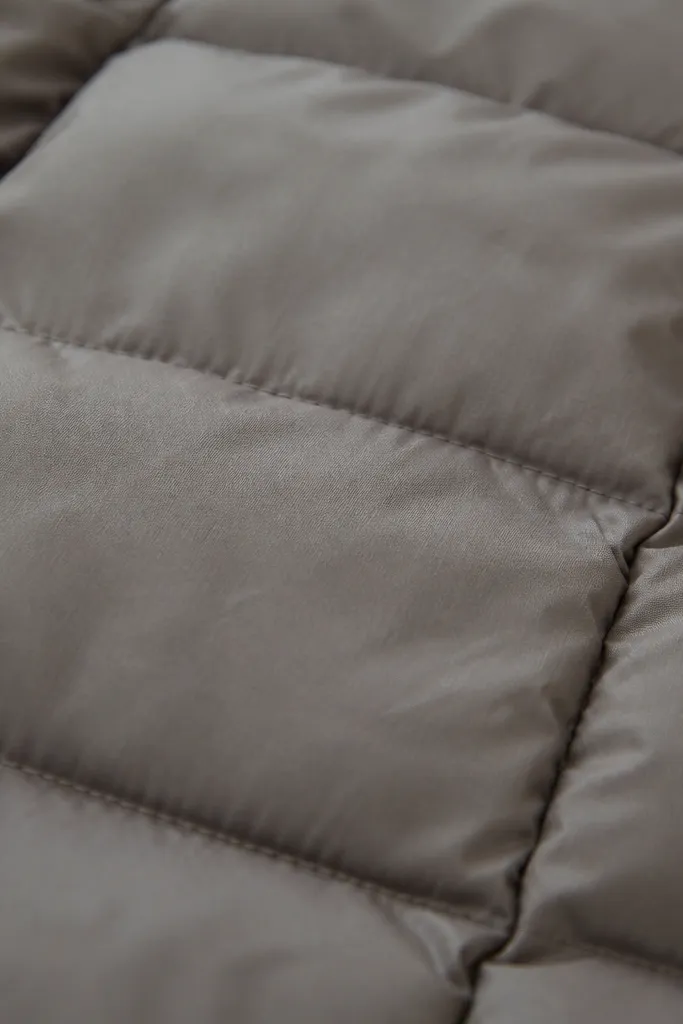 Close-up of a puffer fabric surface showing slight dullness and stiffness; the quilt looks less smooth than a freshly washed example.
