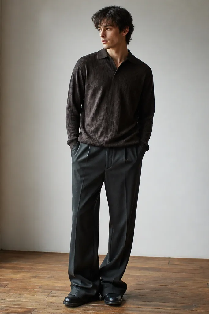 A man in charcoal trousers with extra fabric pooling around the shoes; the hem drags and wrinkles pile up at the front.