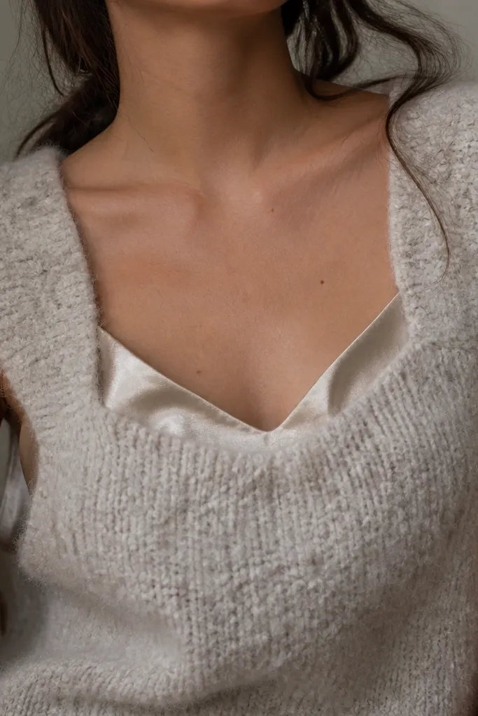 A close photo showing a fuzzy, boucle-like sweater vest layered over a shiny camisole; the different textures clash at the neckline and seams.